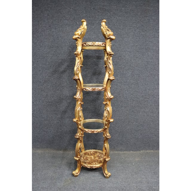 Tall gilt wood and composite etagere display stand with carved scrolling supports and decorative detailing throughout....