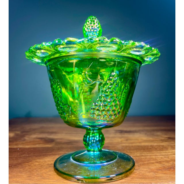 Iridescent lidded green carnival glass candy dish in a grapes and leaves pattern.