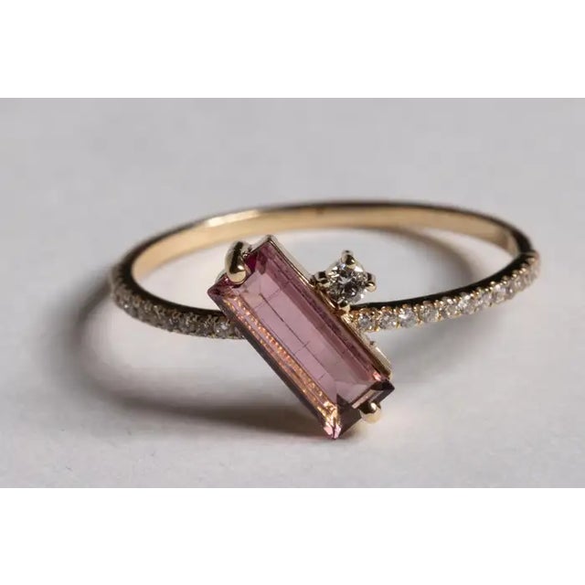 A very unusual 14K gold ring featuring an offset, beveled emerald-cut pink tourmaline gemstone at the center with a round,...