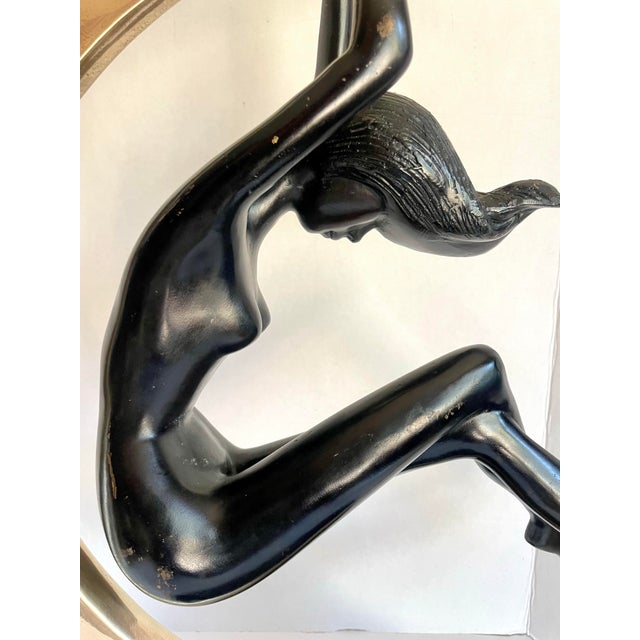Here is a dramatic vintage Art Deco sculpture featuring a graceful female figure suspended within a polished brass...