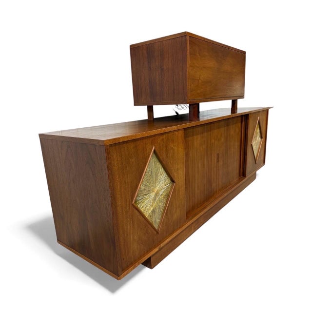 This striking Mid-Century Modern walnut tambour door sideboard and bar cabinet is a true statement piece of 1960s design....