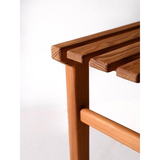 Scandinavian stool from the 1960s in pine with a square base and slatted top, featuring a simple and sturdy design....