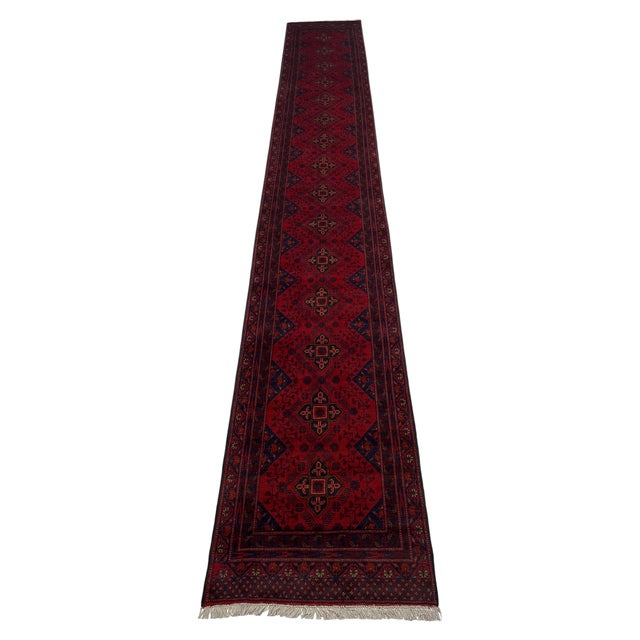 A continuous row of navy geometric medallions runs through the deep red field of this extra-long runner. Small angular...