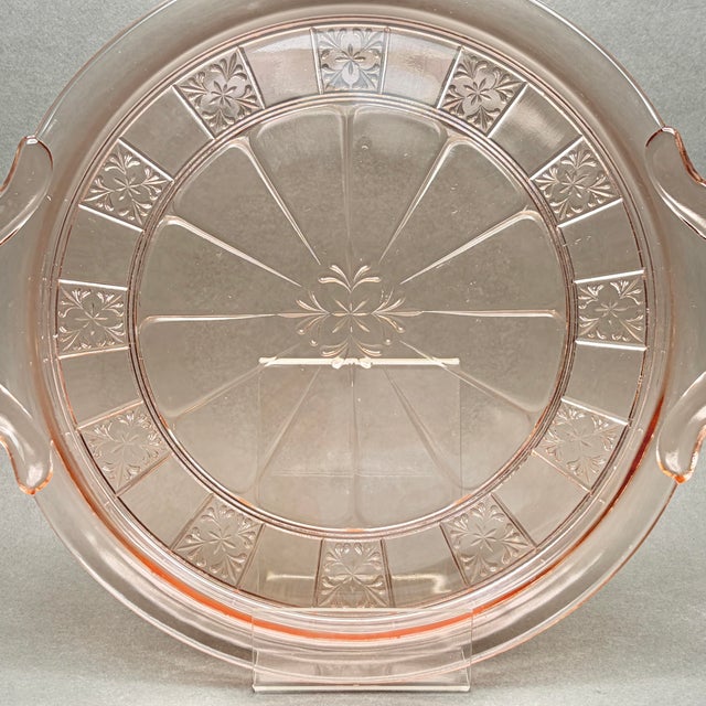 • This striking 1930s pink Depression glass cake plate showcases the classic "Doric" pattern manufactured by the Jeannette...