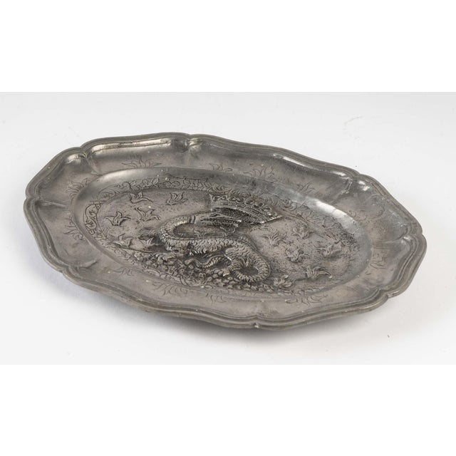 Decorative pewter tray with a crowned dragon motif. Measures: H 2 cm, W 28 cm, D 20 cm.