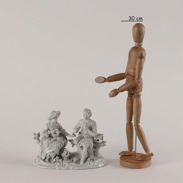White porcelain sculptural group depicting a gallant couple with cage and birds. Under the base the manufacturer's brand....