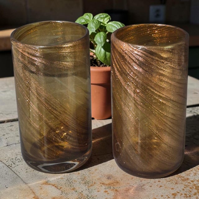 This product is a pair of hand-blown attributed Murano art glass tumblers in a copper and gold color. The contemporary...