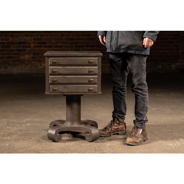 Compact painted-wood cabinet constructed as a square storage box mounted on a turned pedestal base with four scrolled...