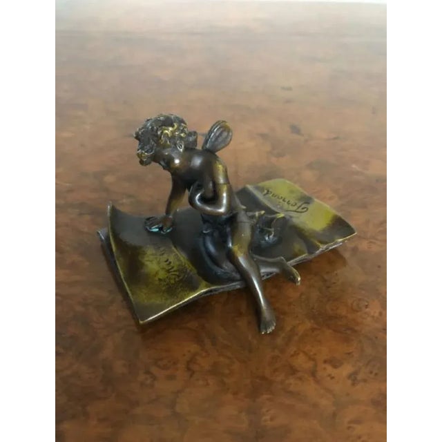 Quality Antique bronze cupid figure signed Ferrand. Quality bronze figure of a cupid setting on a rug signed Ferrand for...