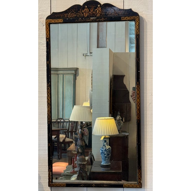 Chinoiserie wall mirror with a shaped crest and painted black frame decorated with gilt figural and landscape motifs. The...