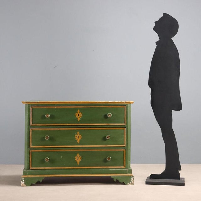 Fir chest of drawers with a green enamel finish. Three drawer fronts with turned wooden knobs and bracket feet. Ochre...