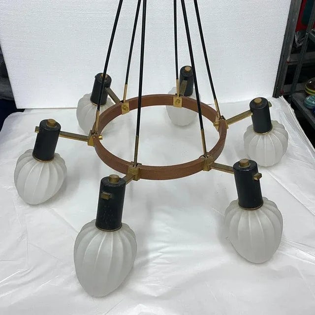 An Italian chandelier made in the Sixties. the round teak structure holds six brass and white opaline glass diffusors, it...