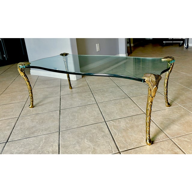 1970s Hollywood Regency cocktail coffee table featuring a thick serpentine shaped glass top supported by four sculptural...