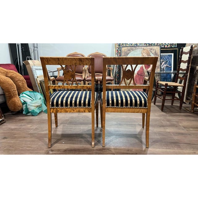 A striking pair of Biedermeier-style armchairs featuring light wood veneers with rich flame/burled grain, elegant curved...