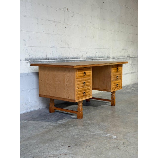 A substantial oak desk by Henning Kjærnulf pairs a broad rectangular top with two banks of three drawers. Sculpted drawer...