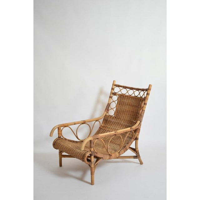 Rattan low armchair, 1950s. Rattan and bamboo low lounge armchair with a woven seat and back, curved scroll details on the...