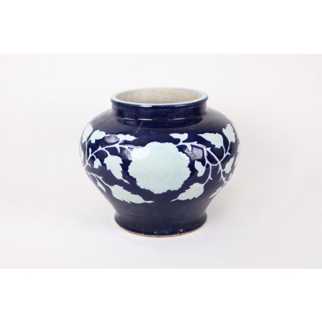 This blue glazed jar with a prominenetly featured white flower features a band of arabesque leaves and vines that wrap...
