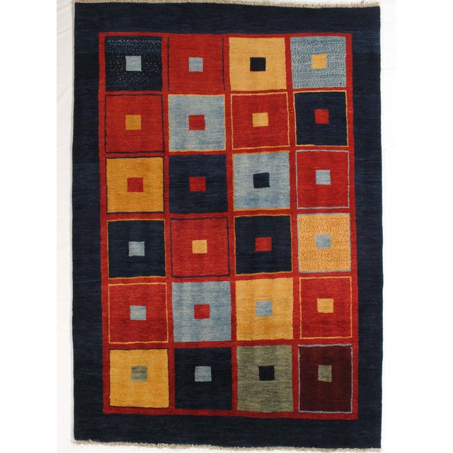 Vintage hand-knotted Persian Gabbeh rug featuring a bold grid of colorful square motifs set within a deep blue field....