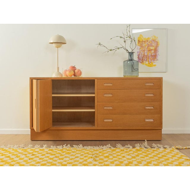 Wonderful sideboard from the 1960s. Corpus in oak veneer with a folding door, two shelves, four drawers and a base typical...