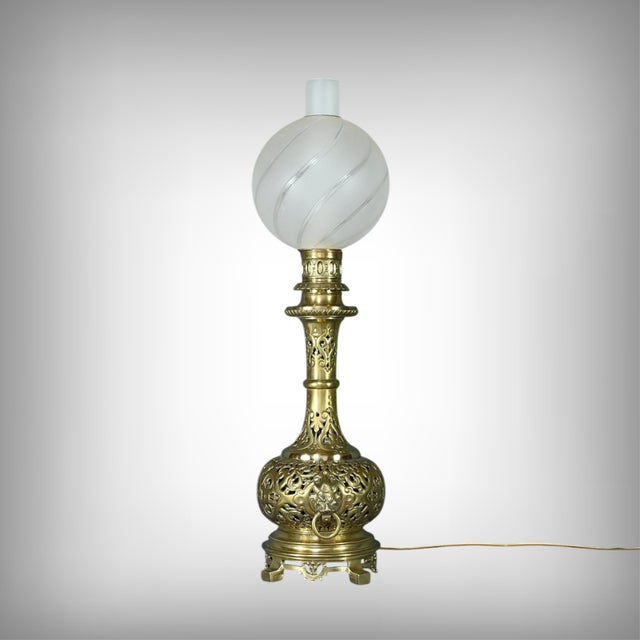 Large electrified oil lamp, made of solid brass, circa 1920. Its openwork stem is adorned with lion heads with rings on...