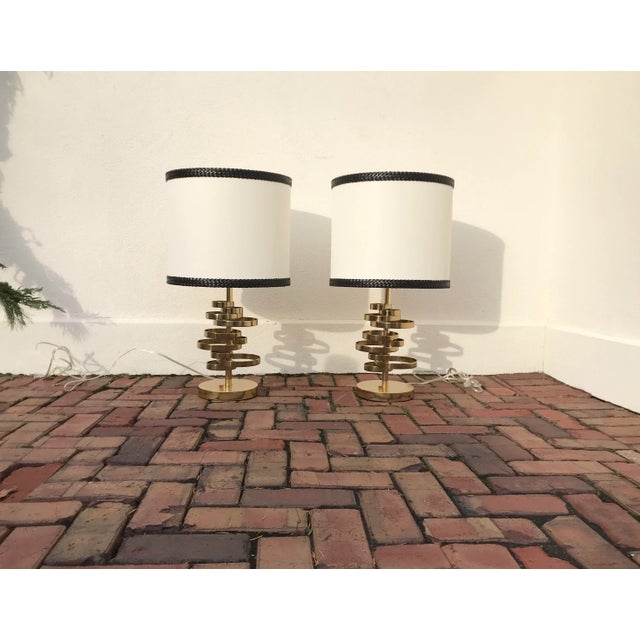 Pair of heavy brass ribbon style table lamps and large white lampshades included with leather like braided trim. Double...