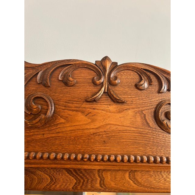 A antique carved hall tree with a lift seat, mirror, and four double pronged hooks. The details and subtle curves give the...