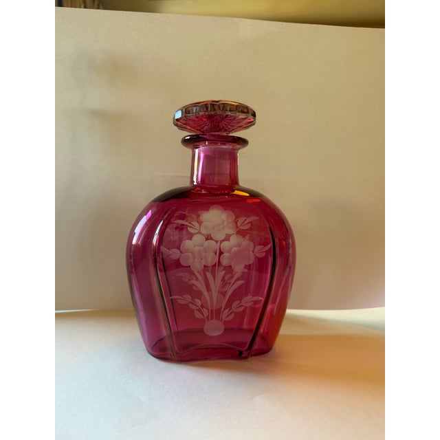 A graceful cranberry glass liquor decanter of flattened, gently waisted form, hand-engraved on the front panel with a...