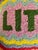 Here is a colorful “Lit AF” decorative pillow by Furbish Studio, featuring a playful hand-hooked design in a vibrant mix...