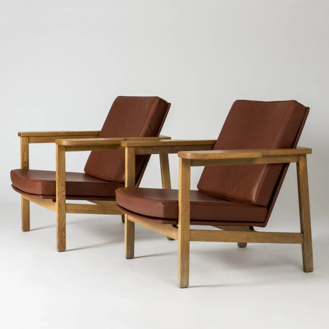 Pair of rare lounge chairs by Carl-Axel Acking in an imposing, luxurious design. Hefty oak frame with wide arm rests and...