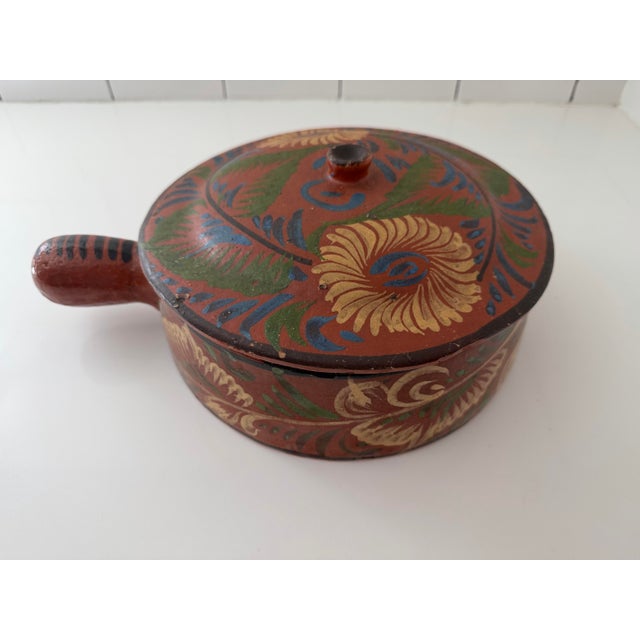 This is a vintage Mexican Tlaquepaque redware pottery lidded bean pot featuring a hand-painted floral motif with a side...