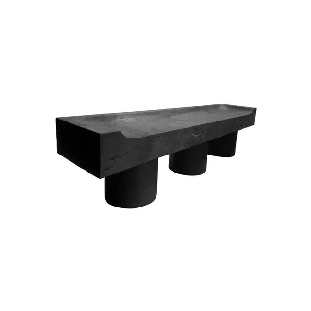 A sculptural bench crafted from solid mango wood, defined by its bold geometry and deeply tactile surface. The elongated...