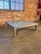 A large and impressive square coffee table featuring a clean parsons-style brushed aluminum frame with a frosted glass...