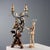 A carved, gilded, and lacquered wooden candelabra. A cherub rests on a triangular base, holding a two-flame iron torch...