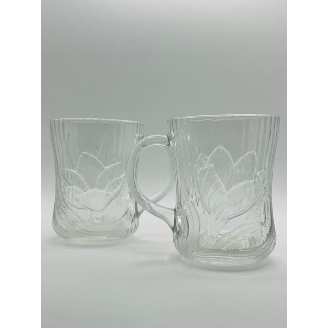 A pair of pressed glass mugs decorated with crocus blossoms amid textured leaves on a clear fluted background with a...