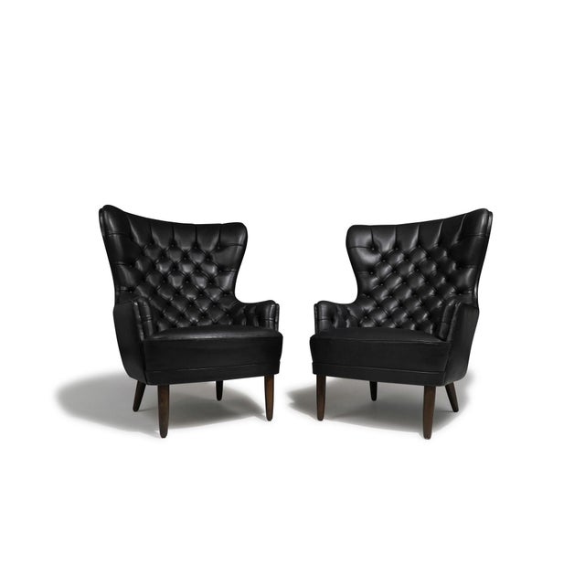 Pair of dramatic high-back armchairs with rounded, sculptural backs upholstered in black leather with classic button-...