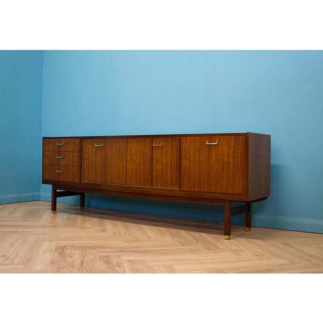 A g plan tola sideboard by e. Gomme, dating from the 1960s. It features brass handles, three drawers including a fitted...