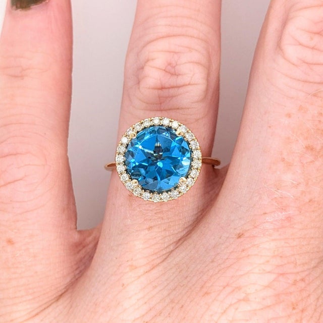 A Swiss topaz sits in a bright sky-blue at the centre of this solid 14K yellow gold ring, surrounded by twenty-five earth-...