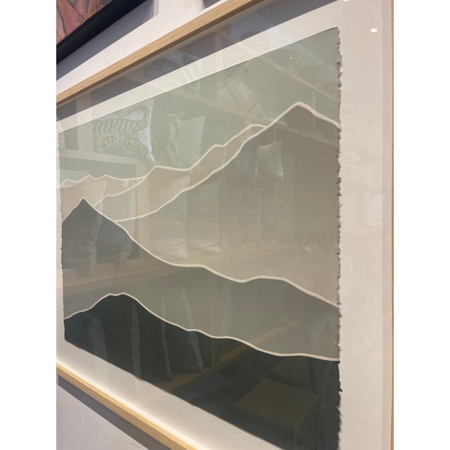 A minimalist lithograph depicting layered mountain forms in soft green and gray tones, outlined with clean white contour...