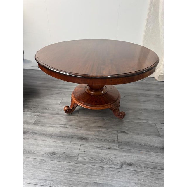Large Regency antique mahogany tilt top dining table featuring a triform base resting on carved pedestal with three...