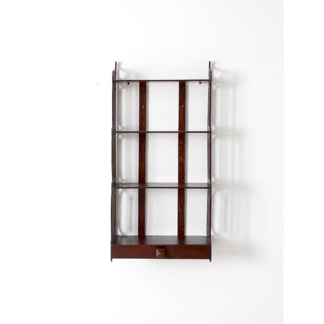 This antique Victorian-era wall shelf features turned spindles, dark wood, and a single drawer, reflecting the Eastlake or...