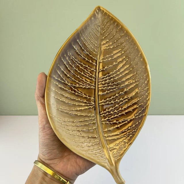 This vintage-inspired dish is crafted from ceramic, featuring a lifelike leaf silhouette with intricate, raised vein...
