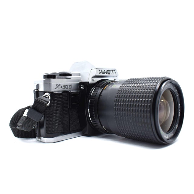This classic Minolta X-370 manual focus SLR offers a sleek, timeless aesthetic with its high-contrast silver and black...