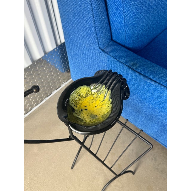 C. 1950s mid-century modern smoking stand. Glazed pottery ashtray in iron frame with magazine rack. Carrying handle at...