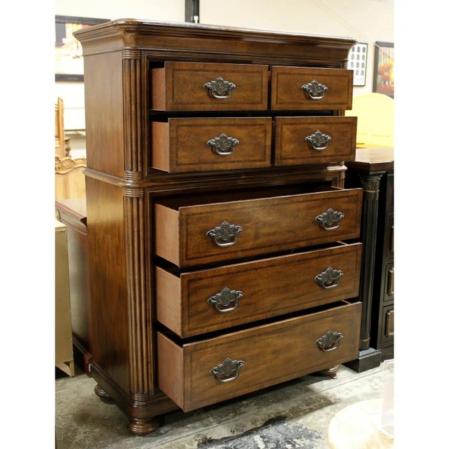 Traditional-style chest crafted in a warm, medium-toned wood finish with decorative moldings, fluted corner details, and...