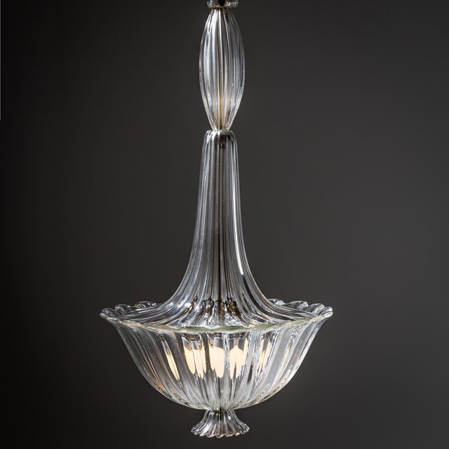 Large pendant light crafted from clear hand-blown Murano glass. The fixture terminates in a basket-shaped, softly...