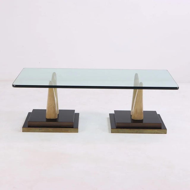 With a rectangular smoked glass top with rounded corners supported on a pair of two "tusks", each on lacquered wood and...