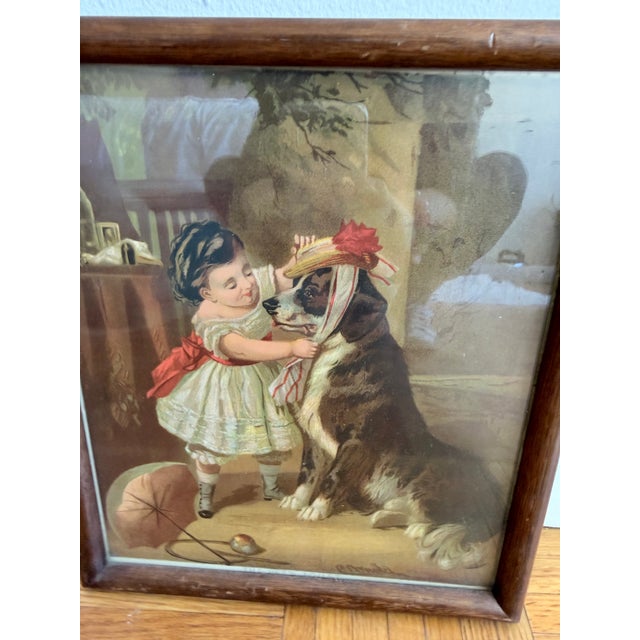 Charming antique/vintage framed color print titled “The Pet’s Toilet,” depicting a young girl playfully dressing her large...