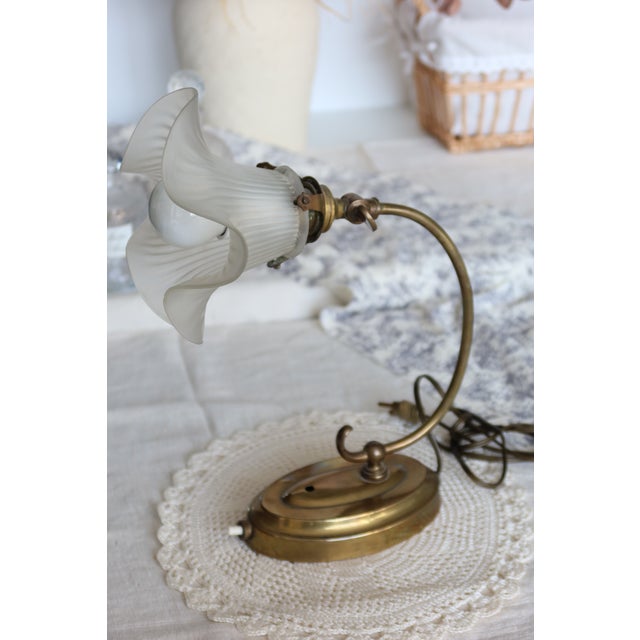 Gold-plated metal table lamp with a curved arm and oval base, topped with a frosted glass tulip shade. The ribbed diffuser...