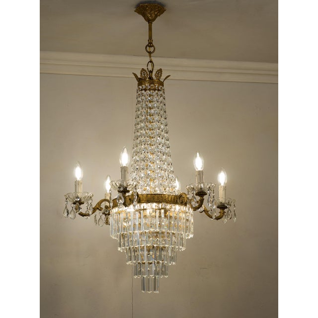 Empire-style chandelier made in Italy in the 1950s–1960s, featuring a brass frame enriched with cut crystals, illuminated...