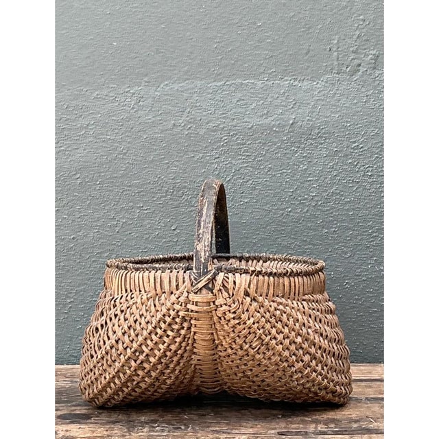 This vintage basket is a gathering-style form with a deep, rounded body that swells outward and narrows slightly at the...